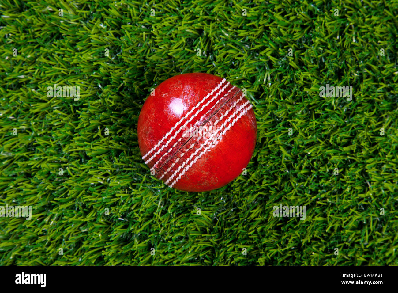 Photo d'une balle de cricket en cuir rouge avec coutures décoratives sur l'herbe Banque D'Images