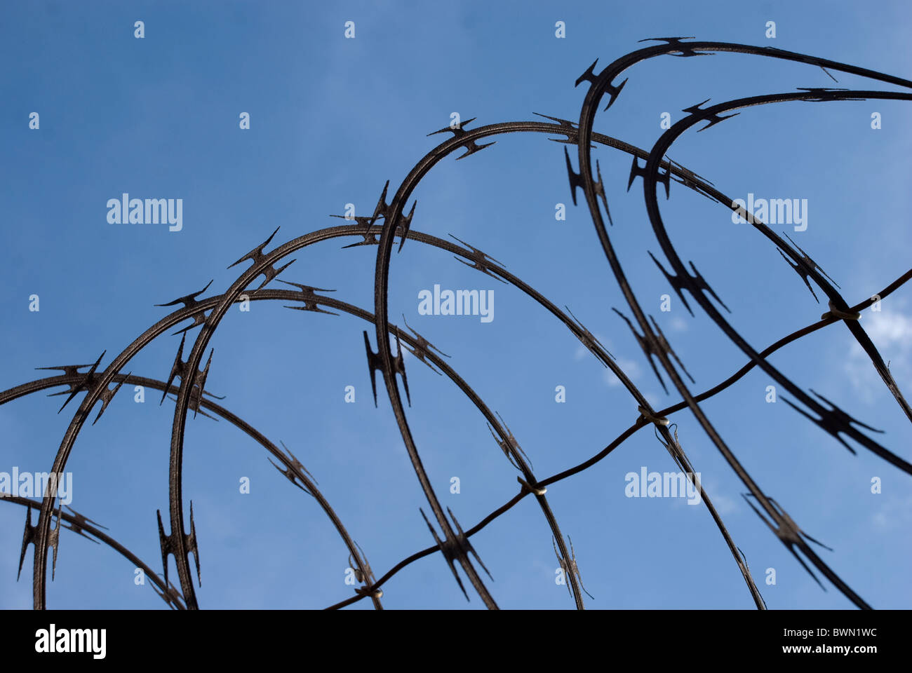 À la recherche jusqu'au ciel bleu clair à travers des barbelés au sommet d'une clôture pour empêcher l'accès de la propriété sur Banque D'Images