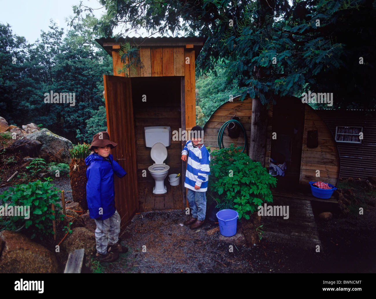 Les enfants debout à côté d'ancienne famille de dunny ou outhouse en pays accueil jardin en Tasmanie Banque D'Images