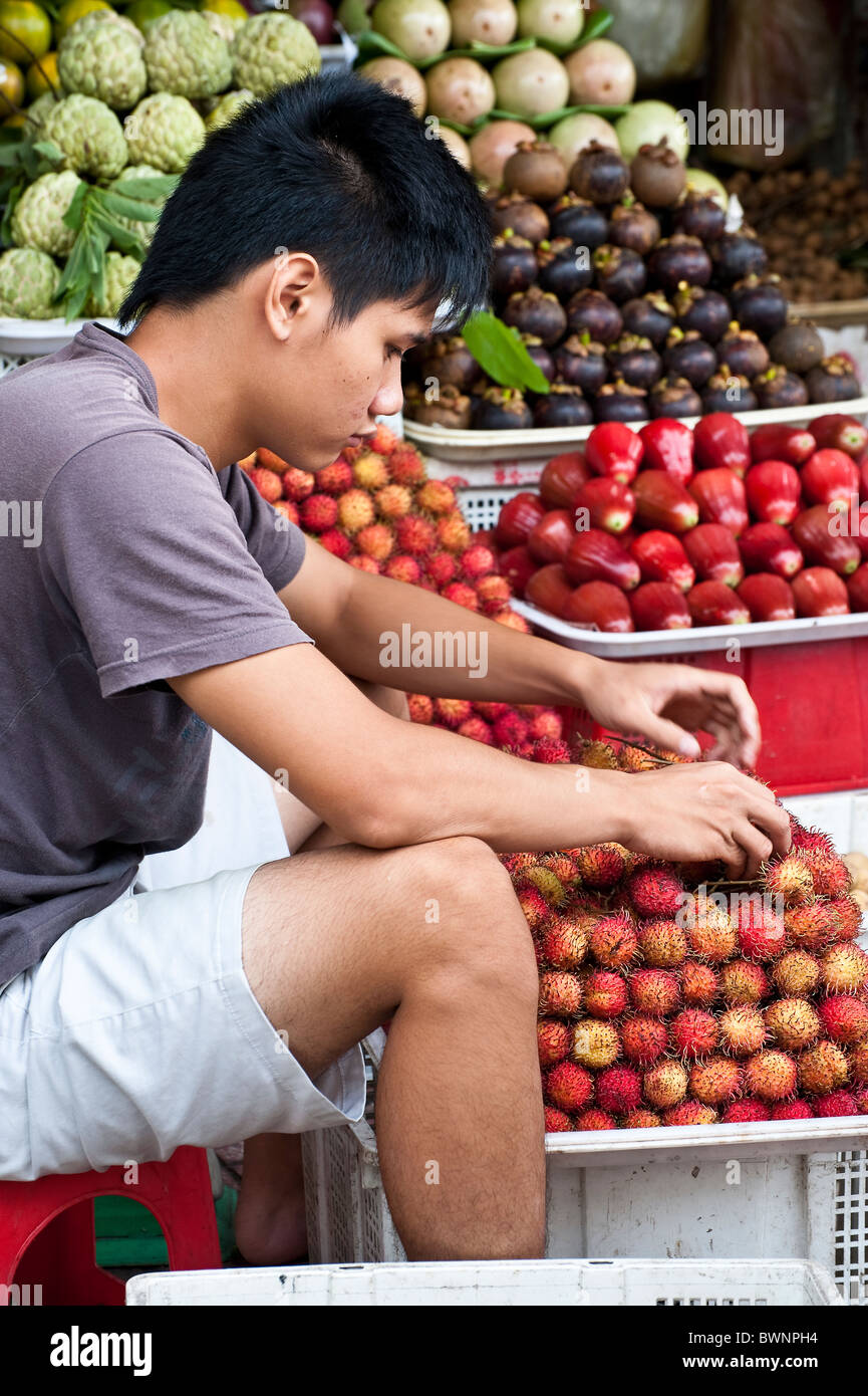 Jeune homme créant une présentation de litchi fruit à un marché de fruits dans les rues de Ho Chi Minh Ville. Banque D'Images