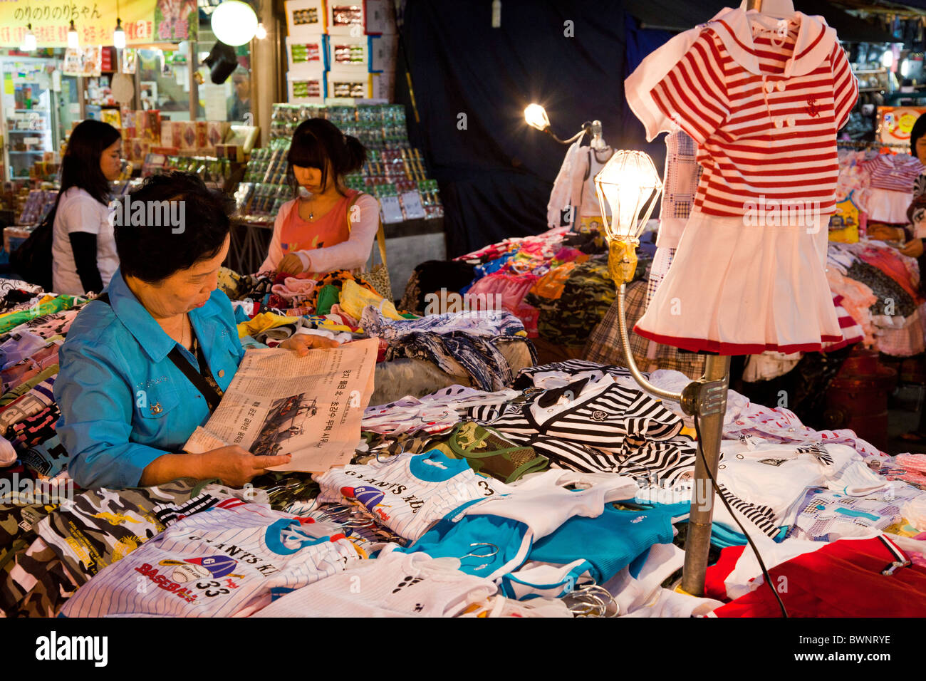 Femme exposant lisant le journal, pour la vente de vêtements dans le marché de Namdaemun à Séoul en Corée du Sud au crépuscule. JMH3858 Banque D'Images