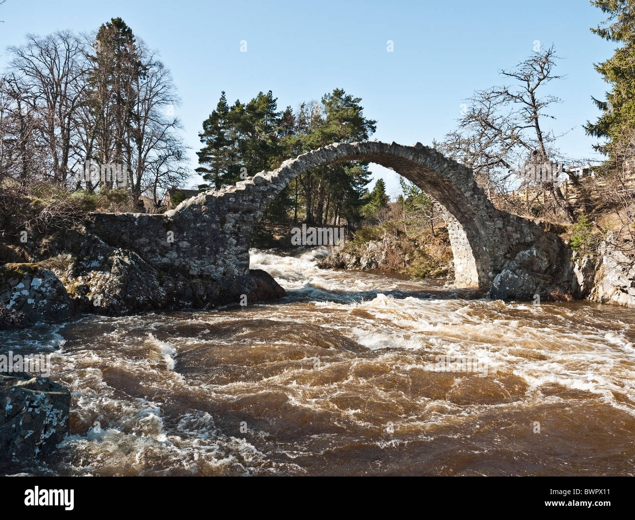 Packhorse vieux pont sur la rivière en crue Boat of Garten avec les eaux de fonte, hiver, Carrbridge, près de Aviemore, Scotland, UK, Cairngorms Banque D'Images