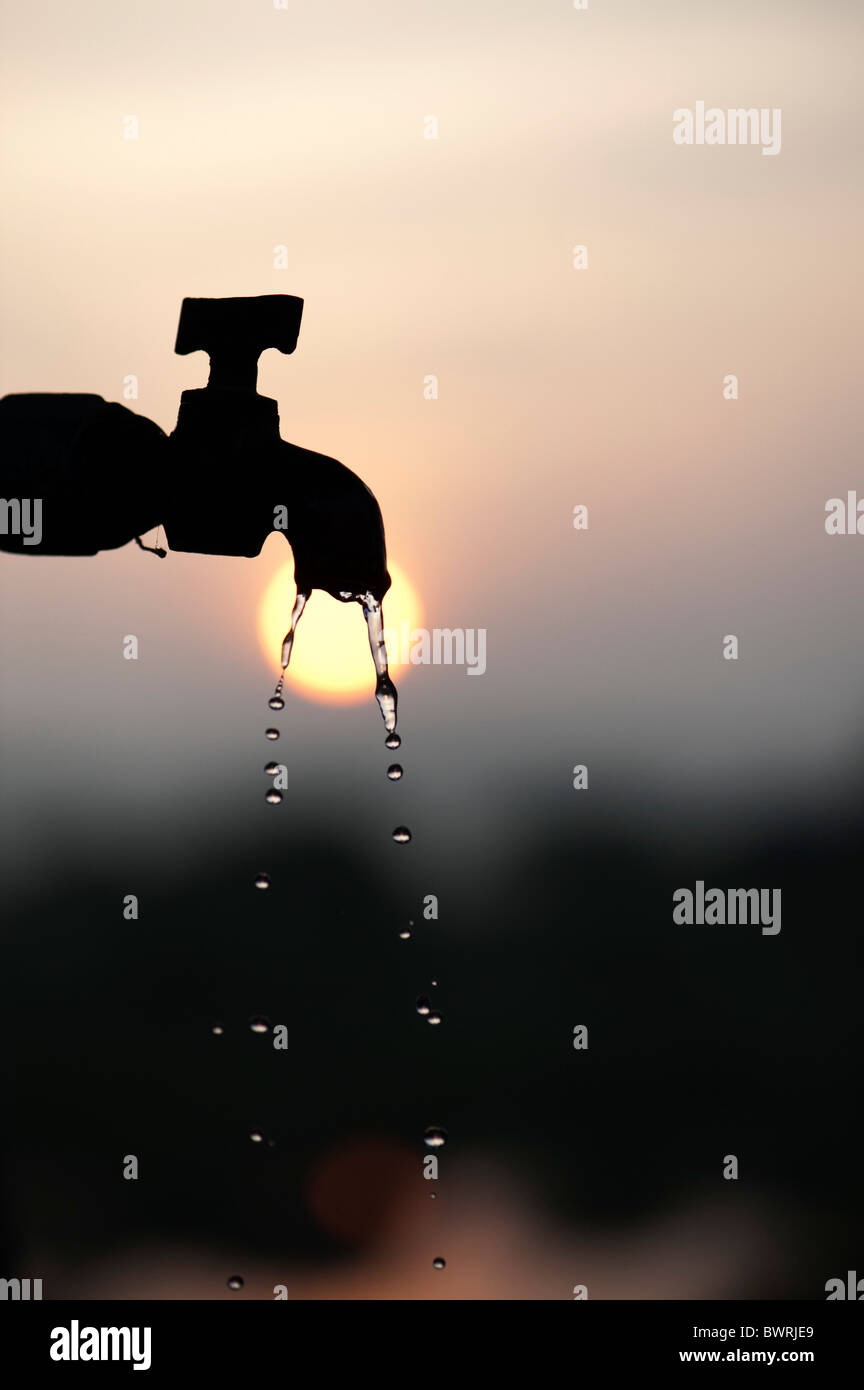 Silhouette d'un robinet de tuyau au lever du soleil avec l'écoulement d'eau Banque D'Images
