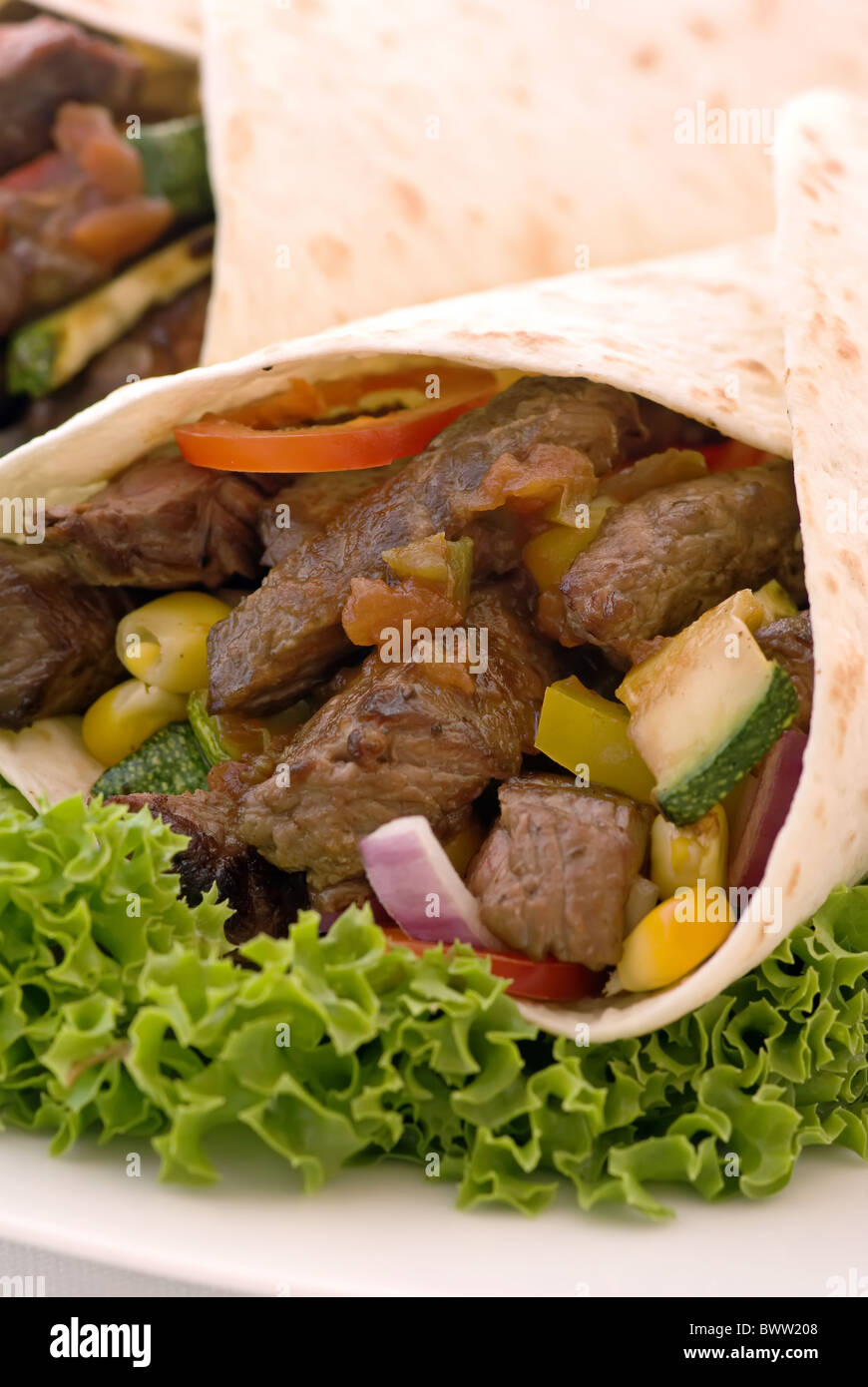 Fajita dans tortilla avec salade et légumes comme gros plan sur une plaque blanche Banque D'Images