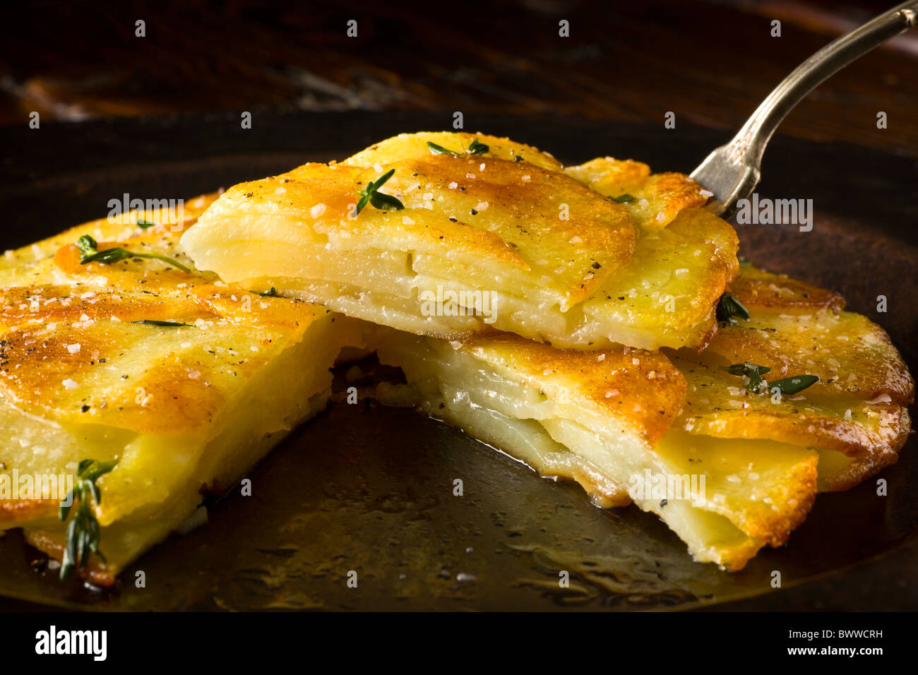 Galette de pomme de terre ou Anna garni de thym frais, sel et poivre et servi sur une plaque rustique. Banque D'Images