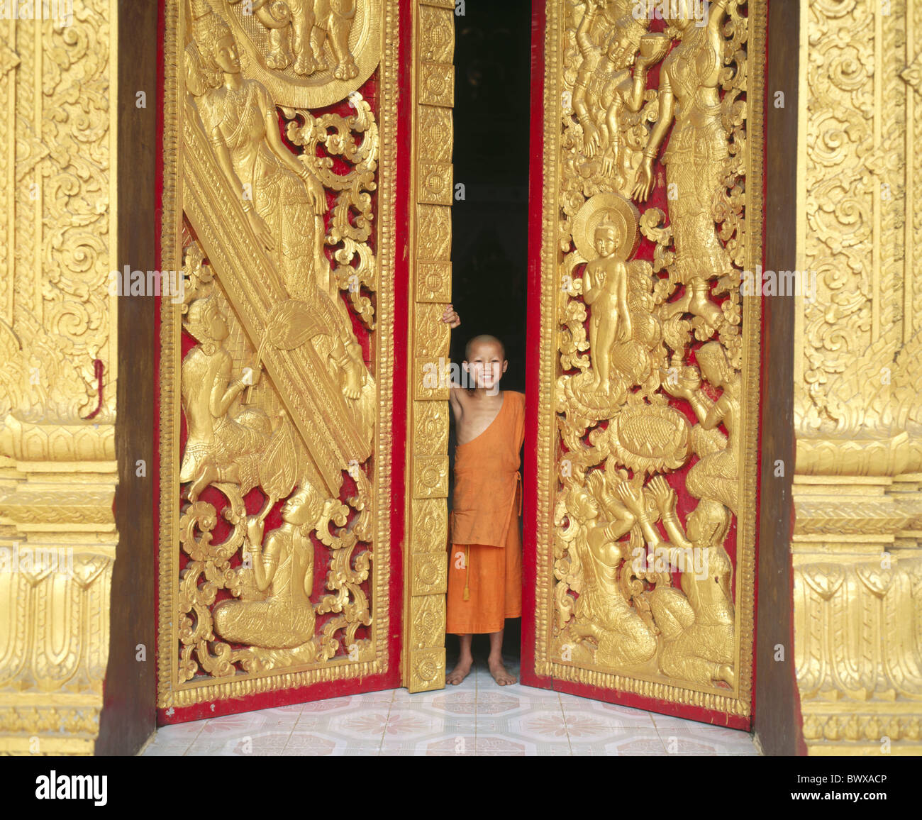 L'écart de la porte jeune Asie Laos Luang Phabang dore modèle presse monk Mönch porte sculptures Wat Manolom Tempel Banque D'Images