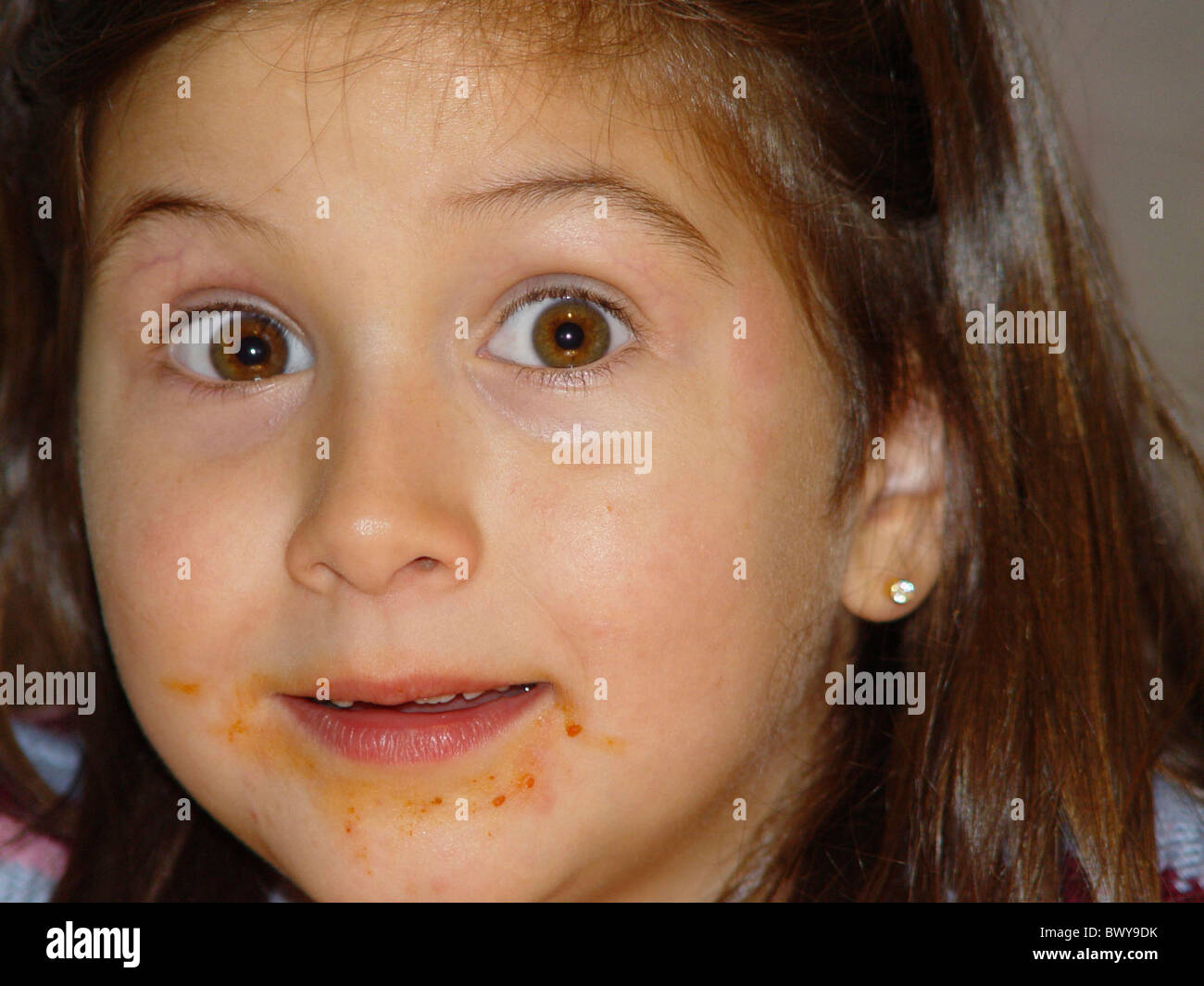 Manger des aliments à l'intérieur de l'expression enfant filles bouche enduite portrait s'étonnent Banque D'Images