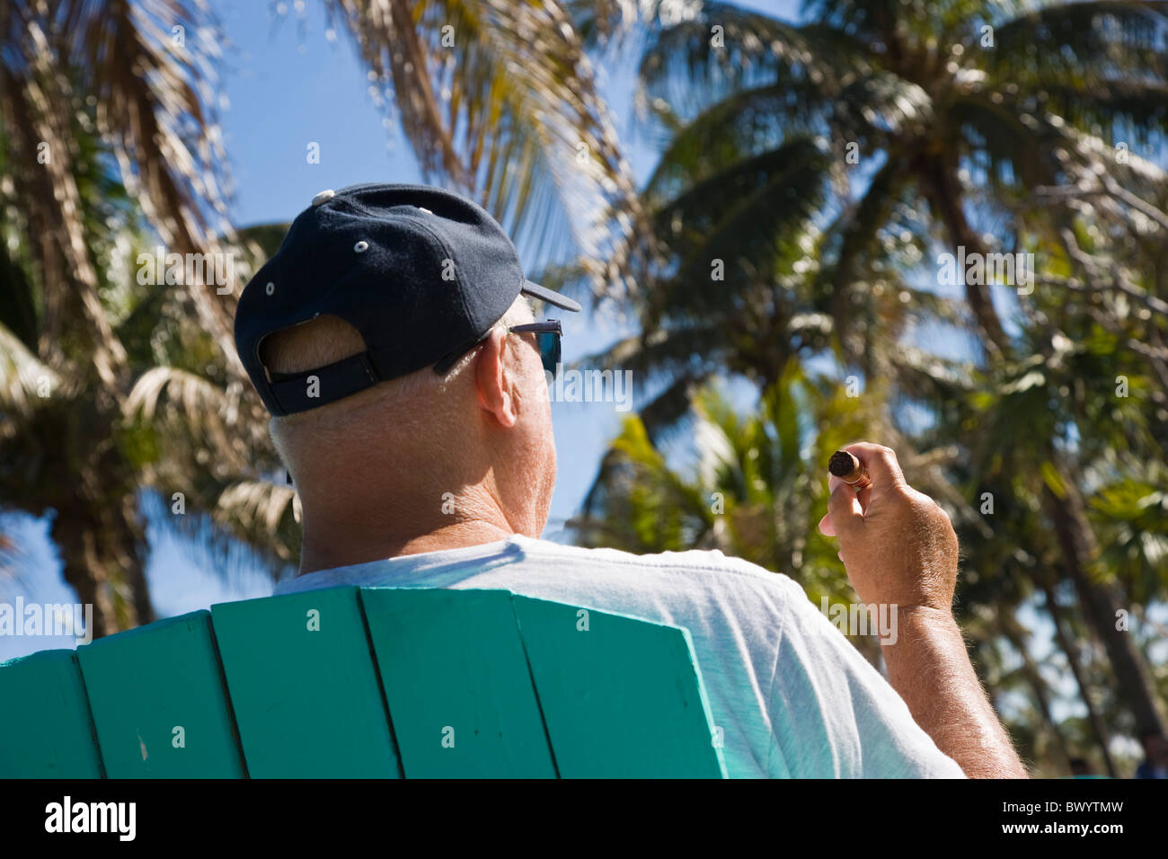 Man fumer un cigare assis sur une chaise à l'extérieur, Miami Beach, Florida, USA Banque D'Images