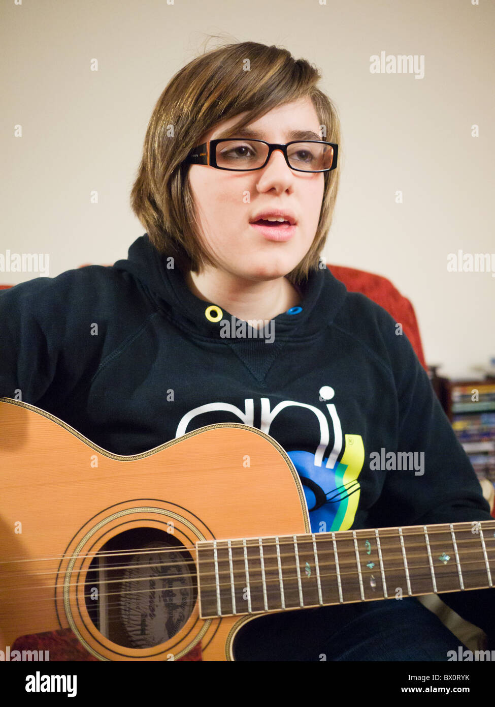 Une jeune fille portant des lunettes, chantant et jouant une guitare  acoustique 12 cordes Photo Stock - Alamy