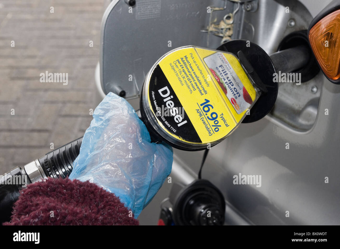 Porter des gants jetables en plastique de l'automobiliste tout en maintenant une pompe à carburant pour remplir un véhicule à moteur diesel à une station de remplissage de gaz. UK Banque D'Images