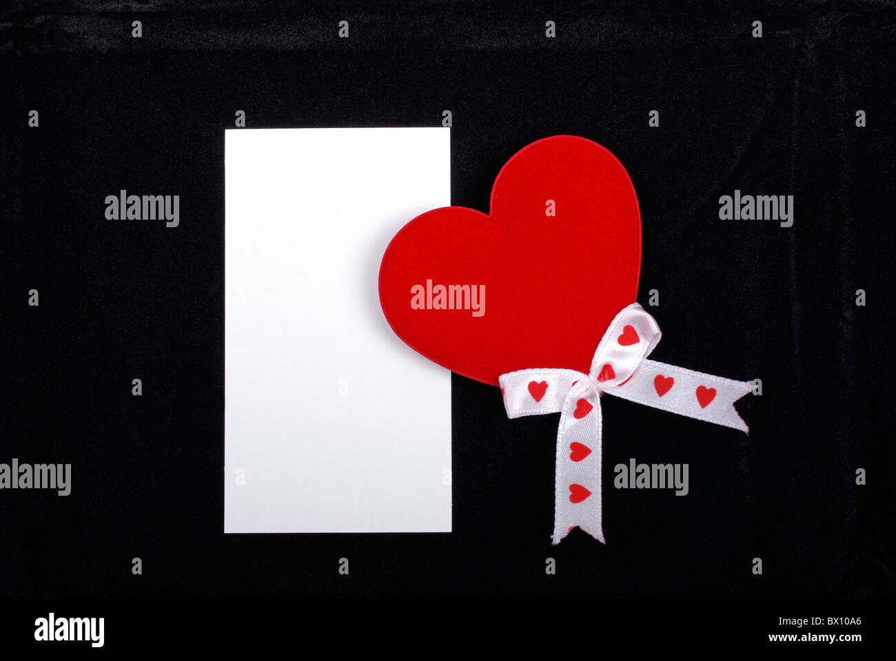 Coeur rouge avec un ruban blanc et une carte vide isolé sur fond de velours noir. Banque D'Images