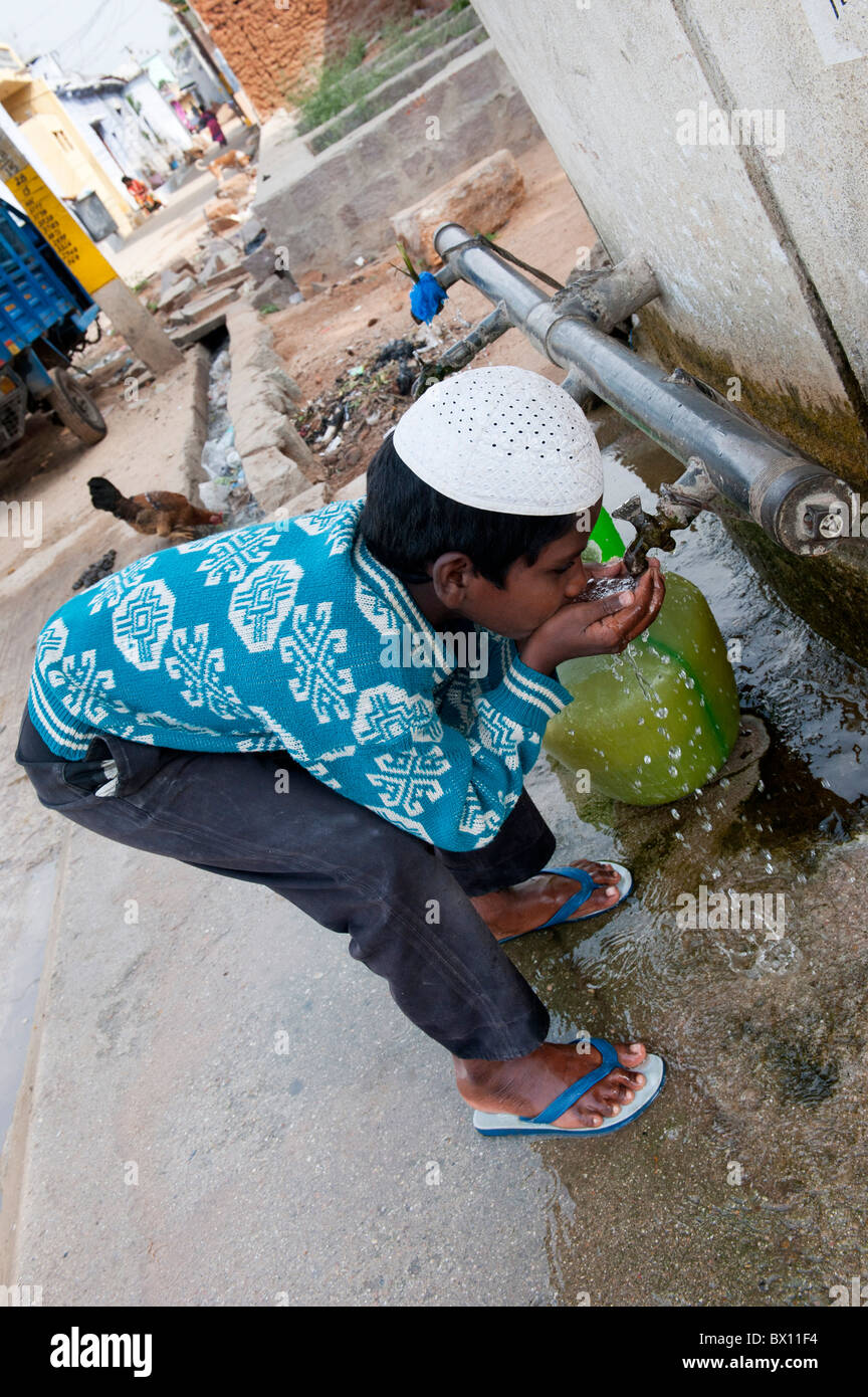 Garçon musulman indien l'eau potable à partir d'un robinet à l'extérieur d'une maison à Bukkapatnam, Andhra Pradesh, Inde Banque D'Images