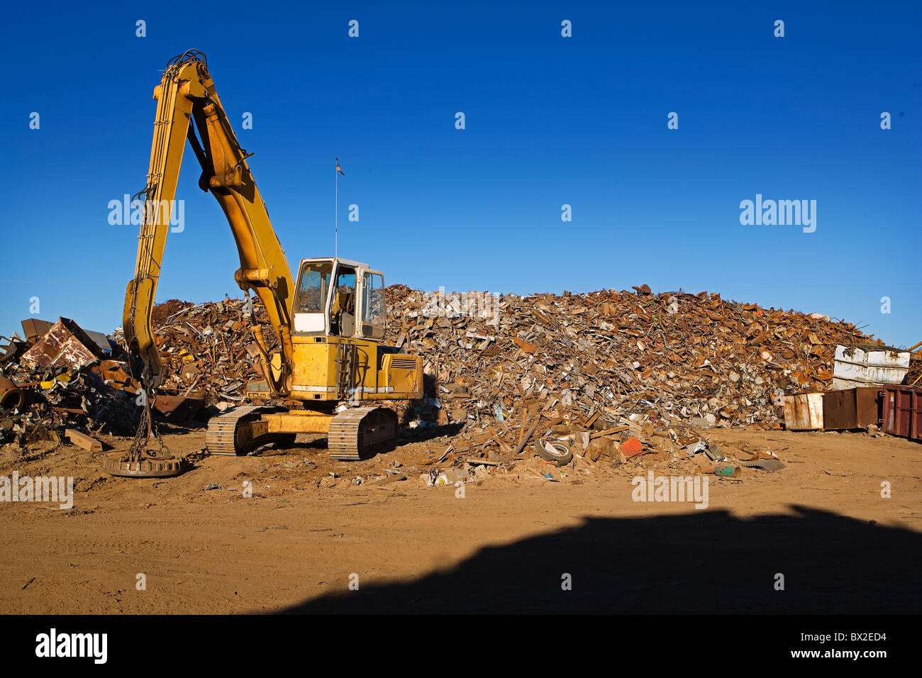 Une grande grue jaune fonctionne avec un énorme tas de ferraille, préparation pour le recyclage sous un ciel bleu. Banque D'Images