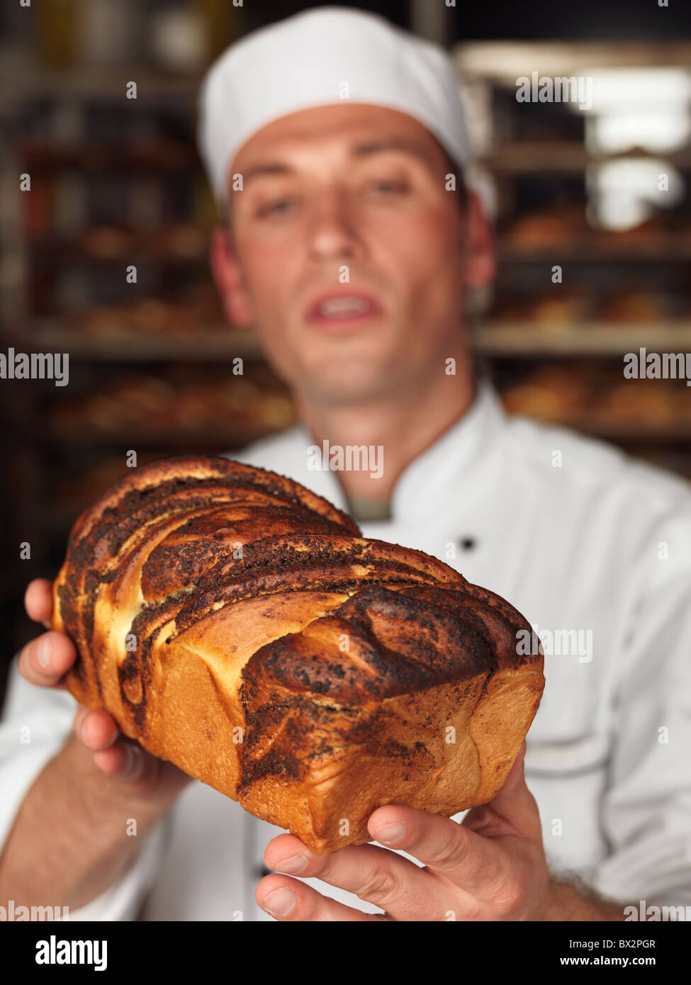 Baker à la recherche d'un pain fraîchement cuit de pain dans ses mains. L'accent est mis sur le pain. Banque D'Images