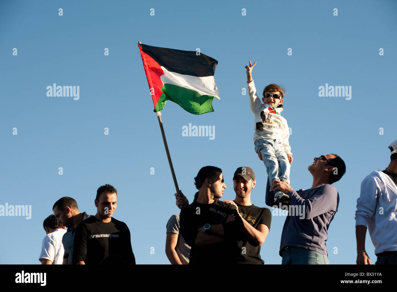 Un garçon palestinien fait un signe de la paix que les protestataires voler le drapeau palestinien lors d'un rassemblement contre les démolitions de maisons par les Israéliens. Banque D'Images