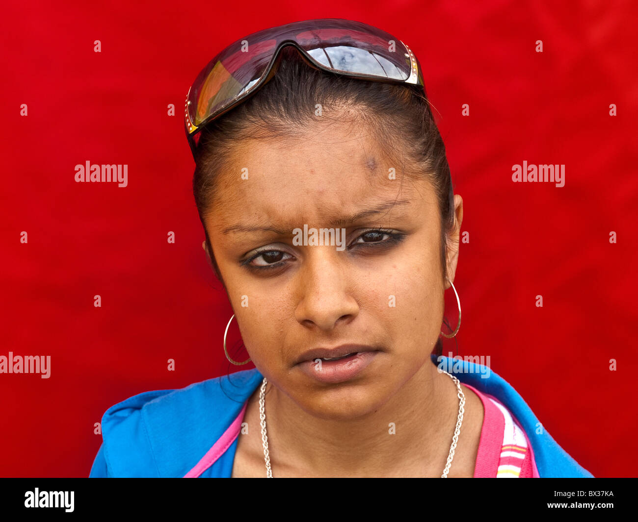 Portrait of Asian Girl wearing sunglasses sur tete de graves (inquiet) expression contre fond rouge. Banque D'Images