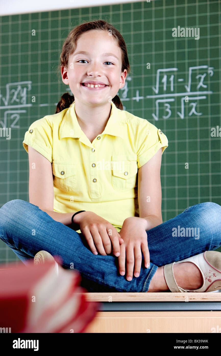 Young Girl sitting on desk in front of blackboard Banque D'Images