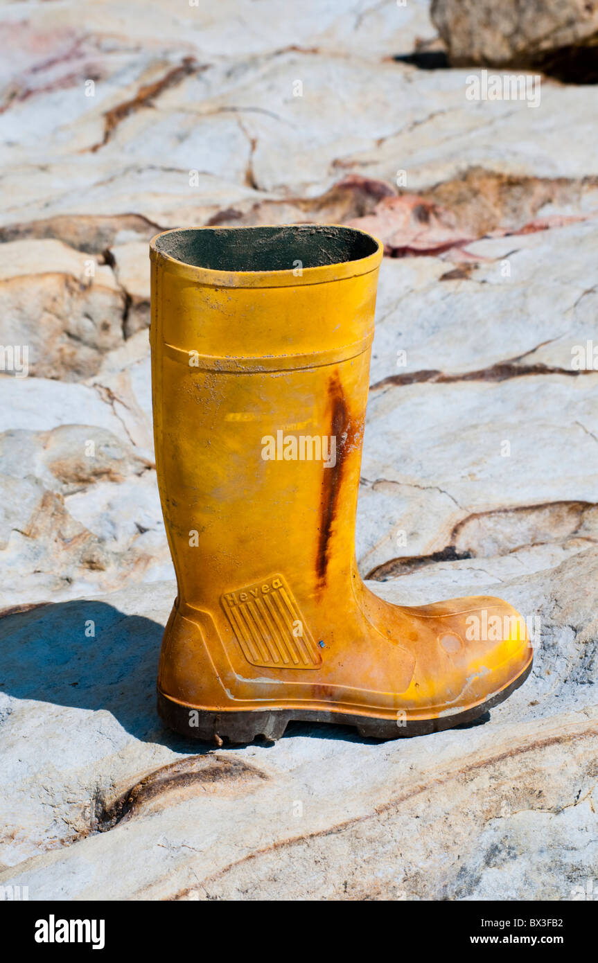 Une vieille botte wellington jaune échoué sur une plage de rochers Banque D'Images