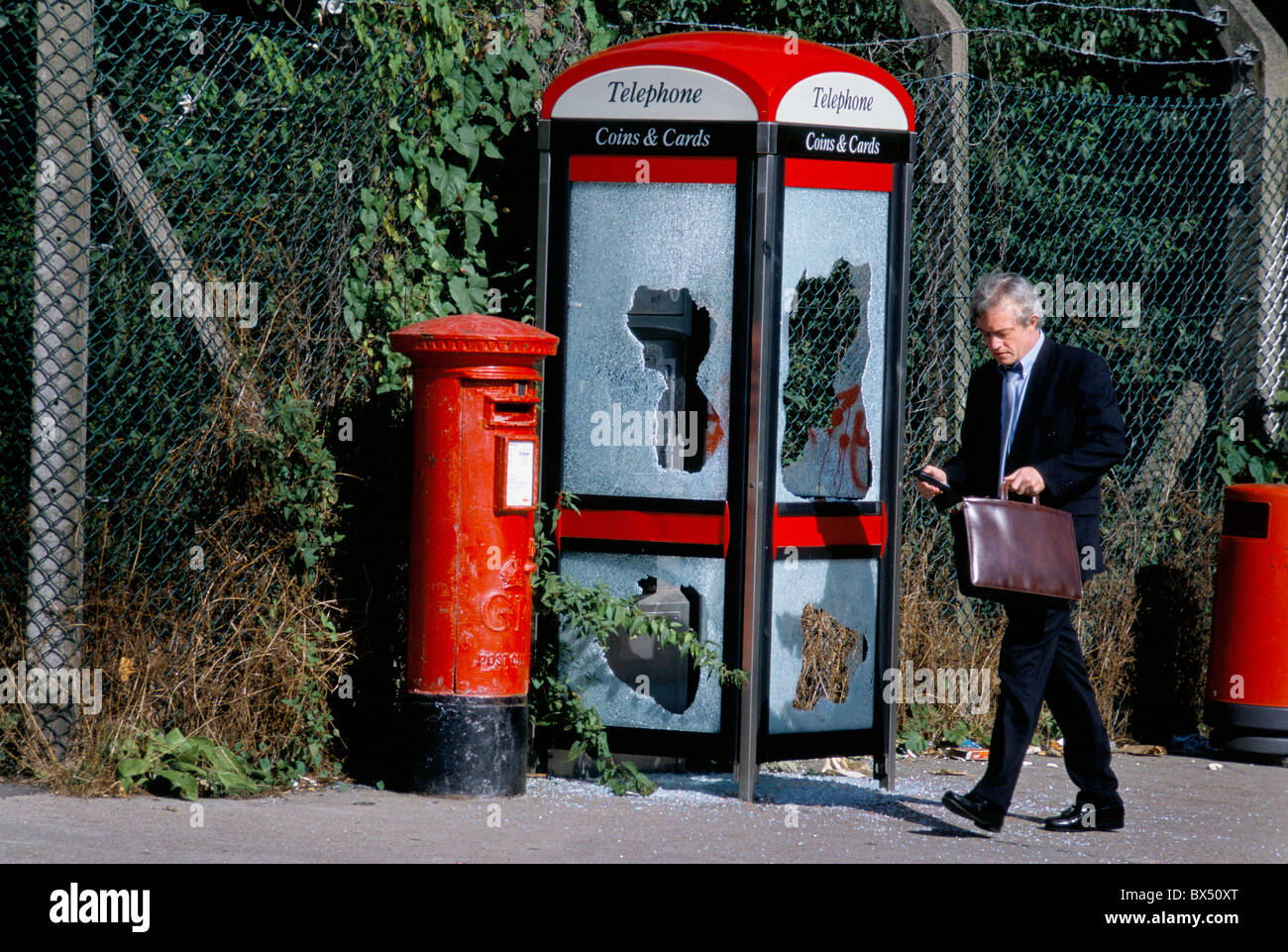 Un homme d'affaires passant un vandalisé British Telecom payphone booth sur une rue du sud de Londres. Banque D'Images