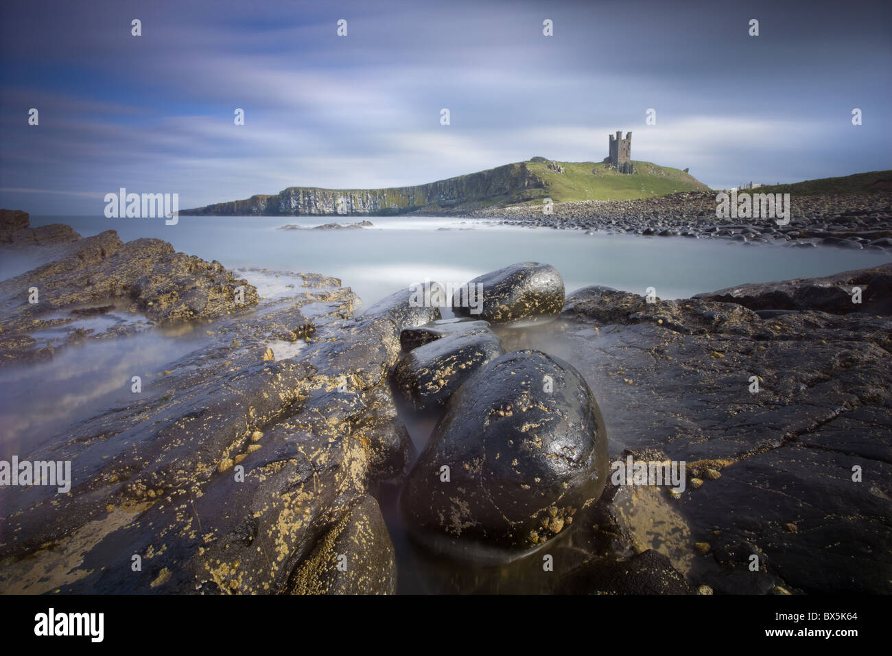 Château de Dunstanburgh baignée de soleil de l'après-midi avec la côte rocheuse en premier plan, Embleton Bay, Northumberland, Angleterre Banque D'Images