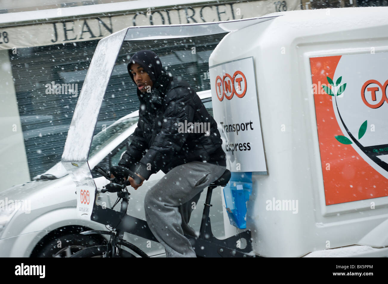 Un homme conduisant un vélo d et la livraison de colis van dans la neige à Paris, France. Banque D'Images