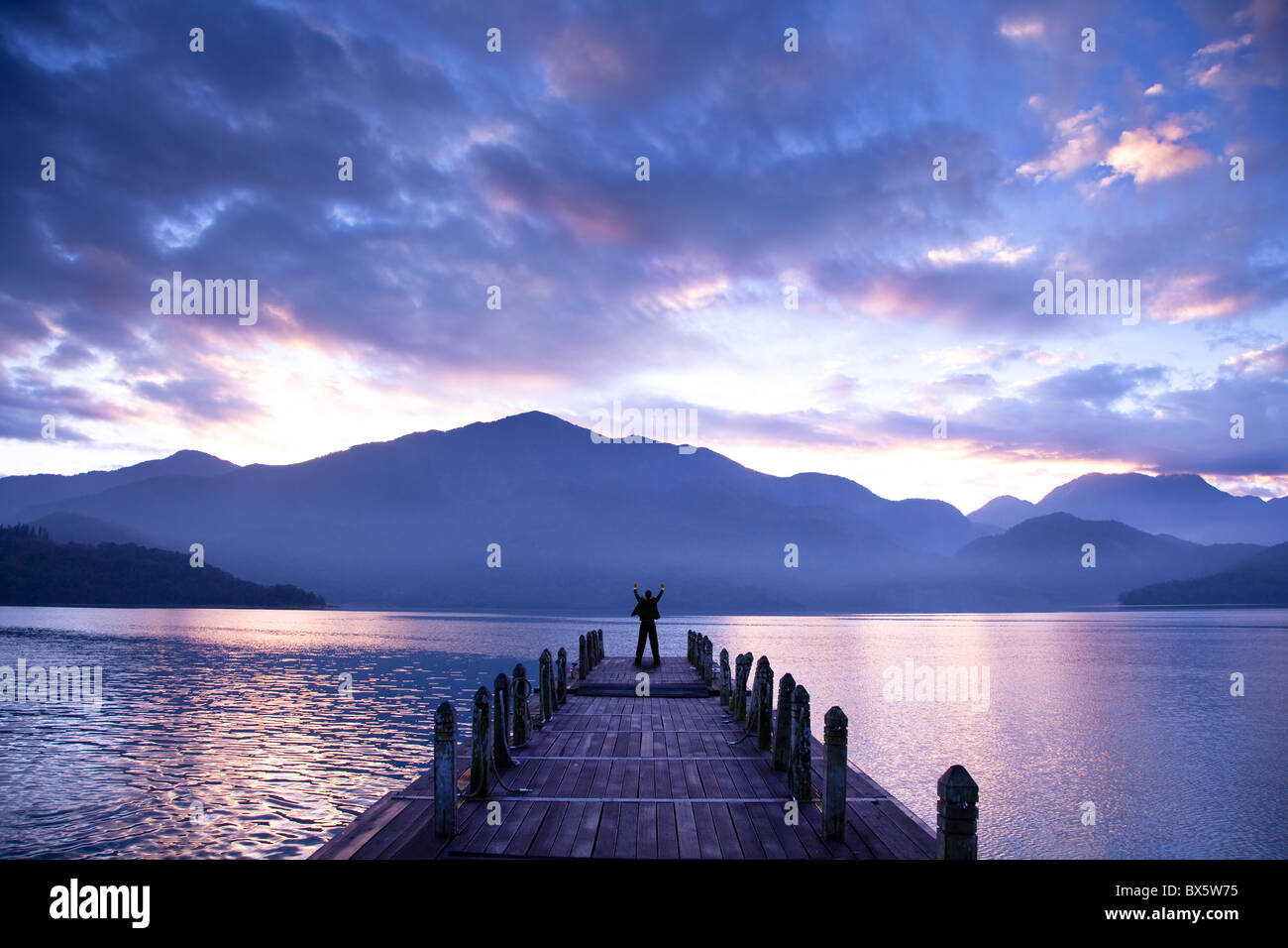 Homme debout sur un quai et regarder les montagnes et le lac Banque D'Images