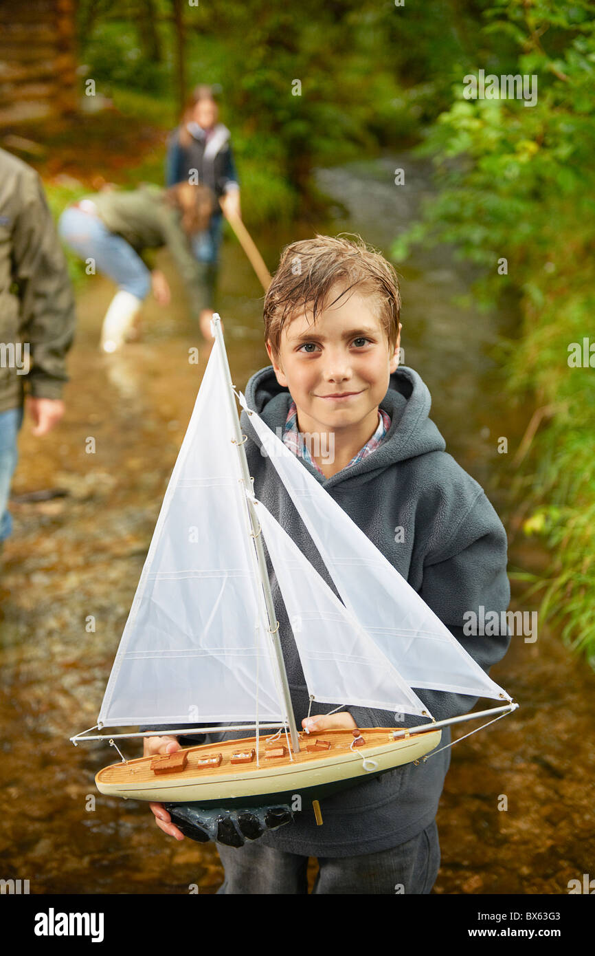 Young boy holding bateau à voile en rivière Banque D'Images