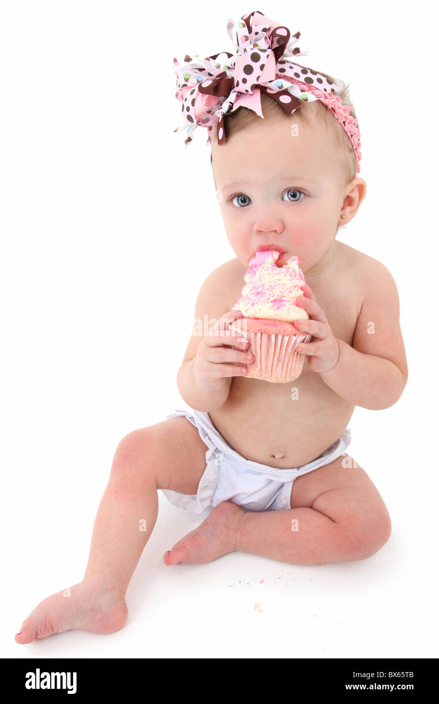 Adorable bébé de 10 mois girl eating cupcake glaçage rose sur fond blanc. Banque D'Images