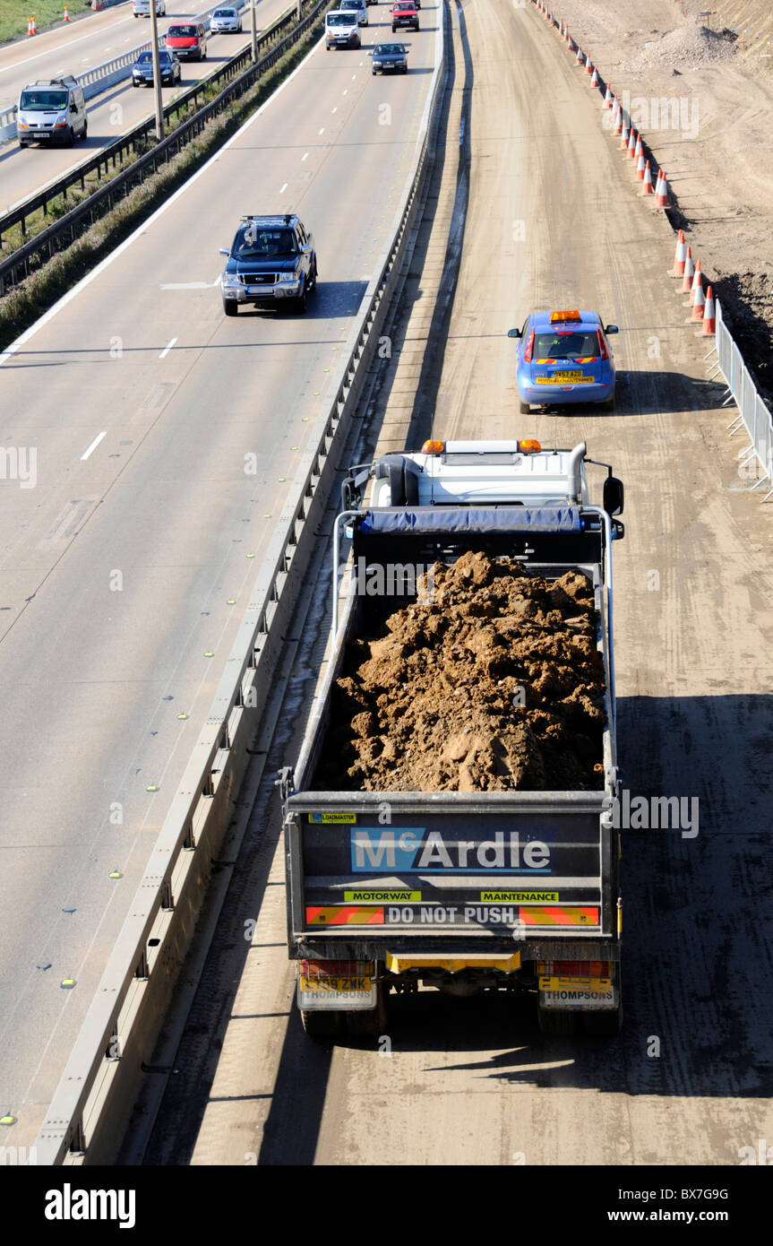 Camion benne travaillant sur l'élargissement de l'autoroute M25 en acier protégé par des barrières de collision Banque D'Images