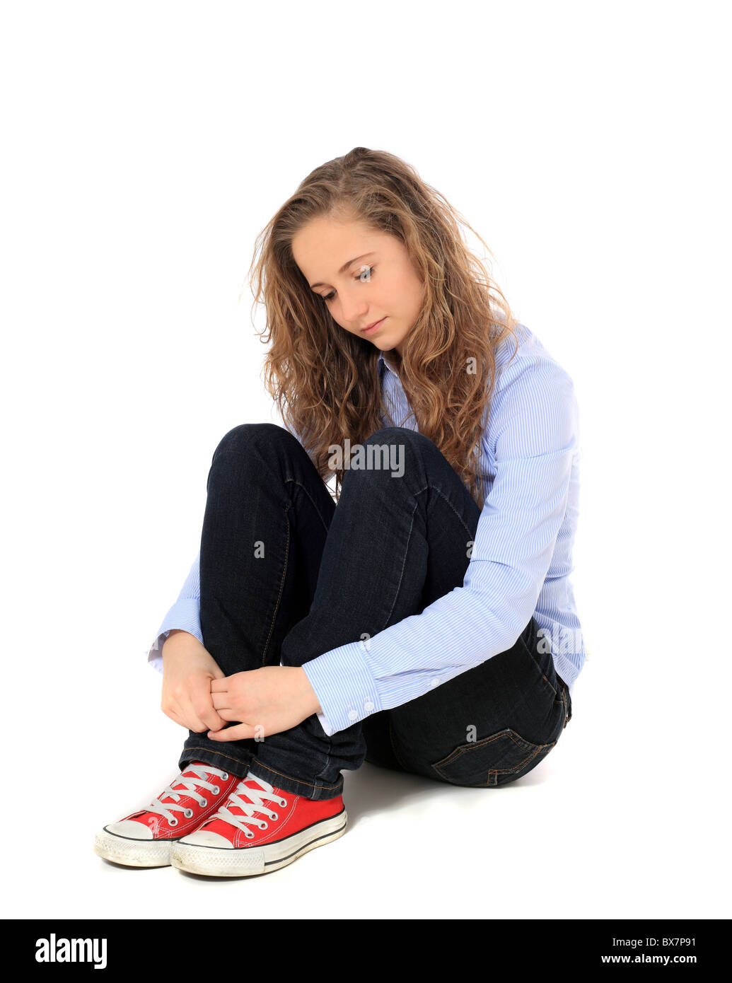 Triste jeune fille assise sur le sol. Le tout sur fond blanc. Banque D'Images
