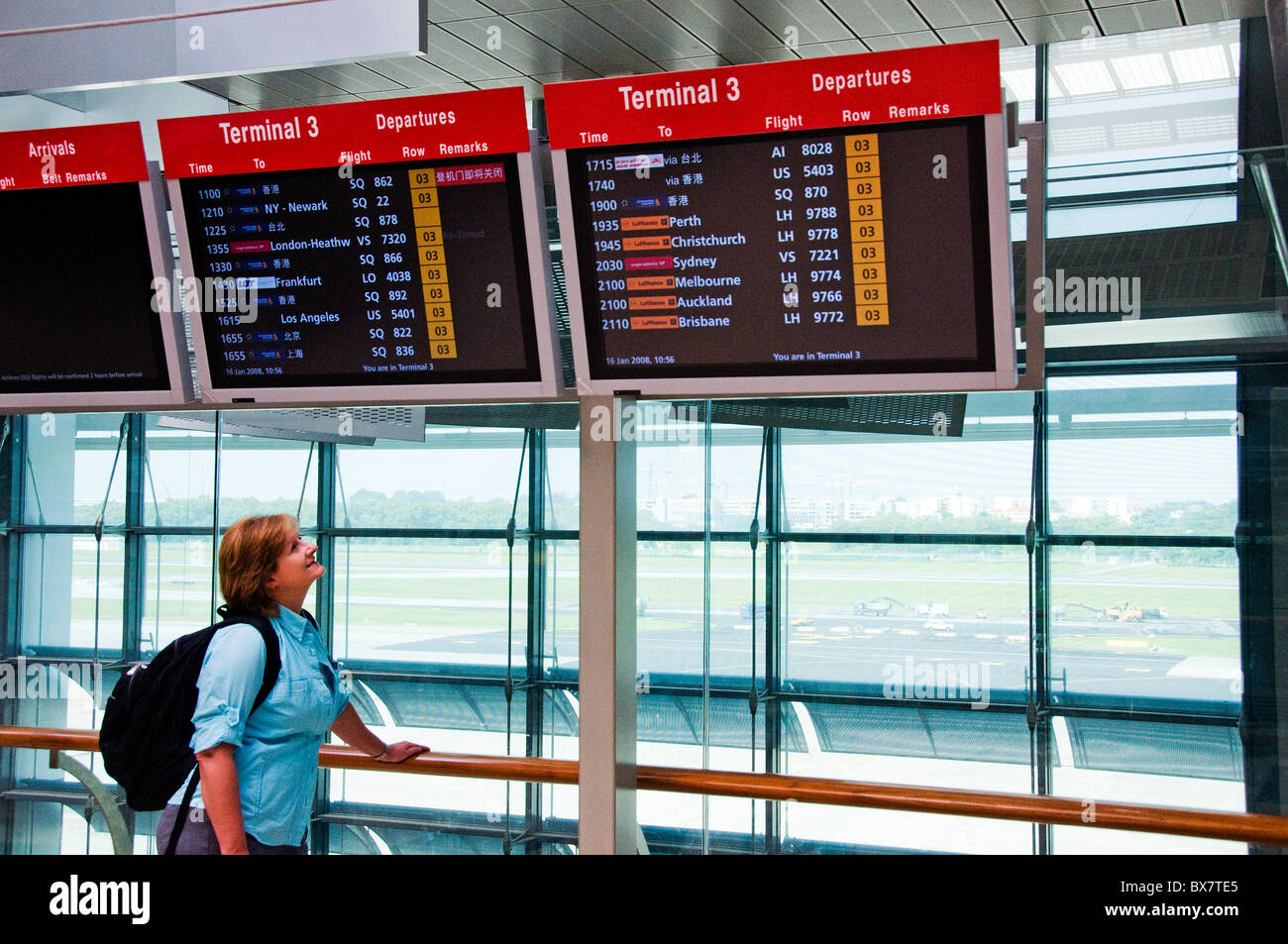 Femme debout et l'affichage des moniteurs CRT pour les heures de départ et d'arrivée à l'aéroport moderne à Singapour Asie du sud-est Banque D'Images