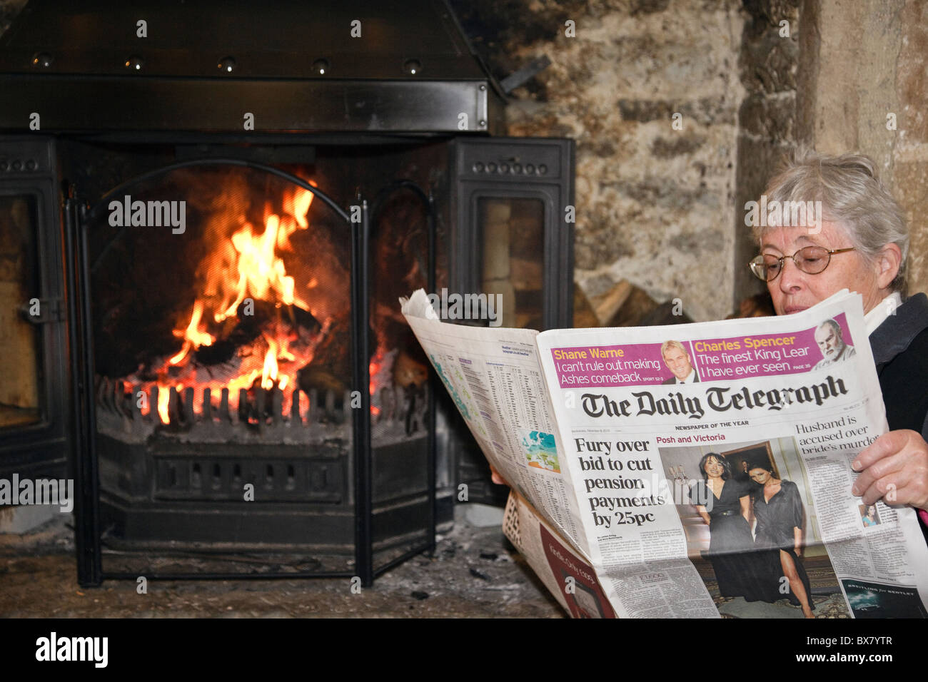 Retraité Retraité Senior woman reading a Daily Telegraph Journal journal déclaration des impôts par un feu de cheminée à l'intérieur. En Angleterre, Royaume-Uni, Angleterre Banque D'Images