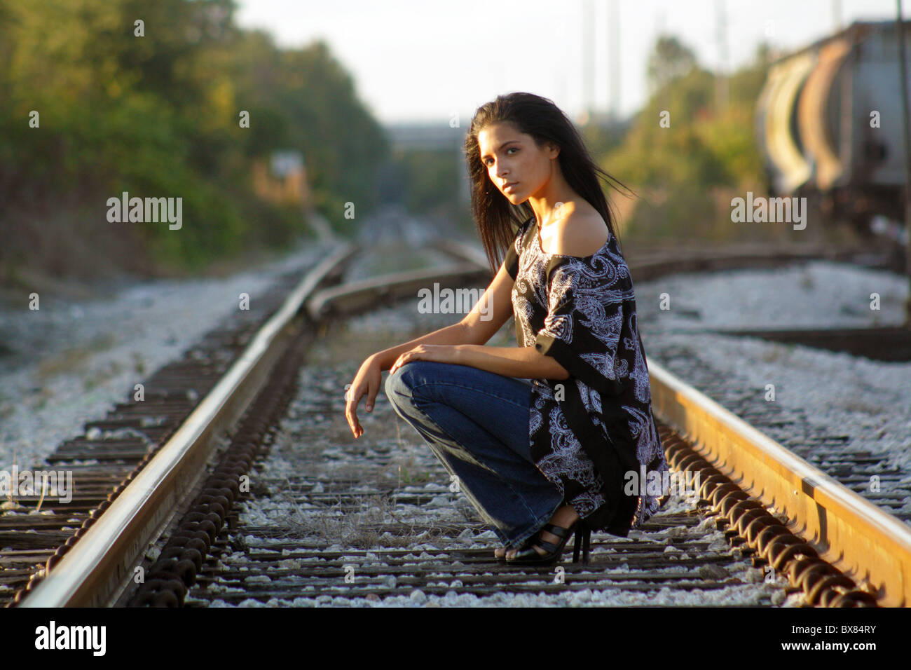 Une belle latina adolescents s'accroupit sur une voie ferrée, regardant la caméra. Banque D'Images