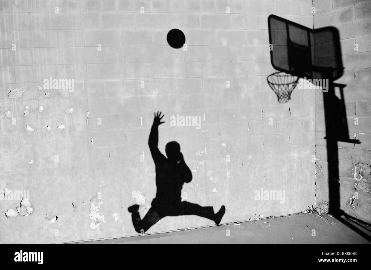 Une silhouette d'un homme le tournage d'un basket-ball, dans le contexte d'un mur de briques avec de la peinture, dans une aire de jeux. Banque D'Images