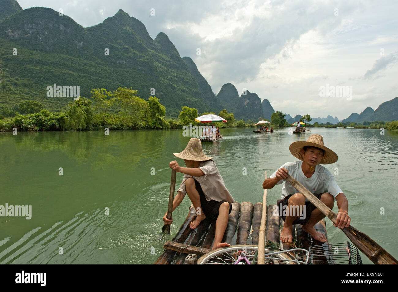 Couple chinois transportant des touristes le long de la rivière Yulong sur un radeau en bambou, Yangshuo, Guangxi, Chine. Banque D'Images