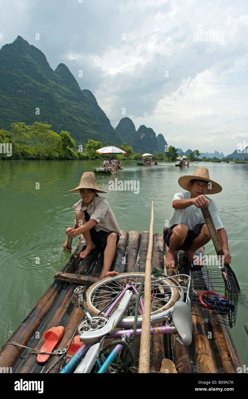 Couple chinois transportant des touristes le long de la rivière Yulong sur un radeau en bambou, Yangshuo, Guangxi, Chine. Banque D'Images