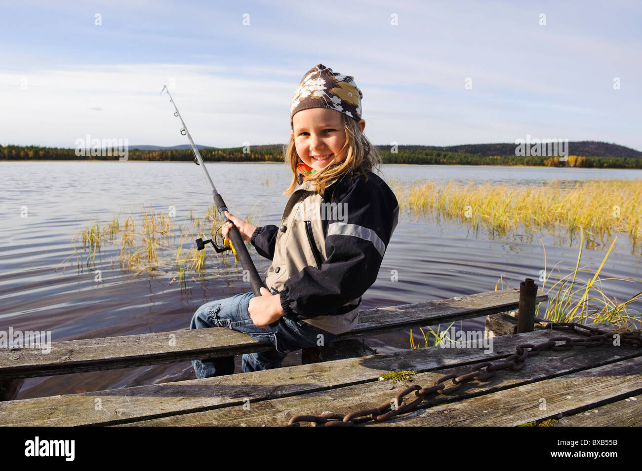 Portrait of smiling girl sitting on jetty avec canne à pêche Banque D'Images