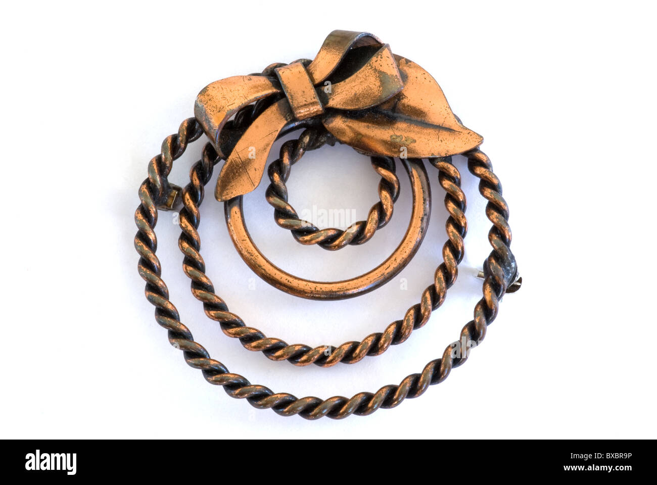 Broche ou broche en cuivre des années 1950 vintage de forme circulaire avec un noeud attaché au sommet. La goupille ressemble à une forme moderne de couronne. Banque D'Images