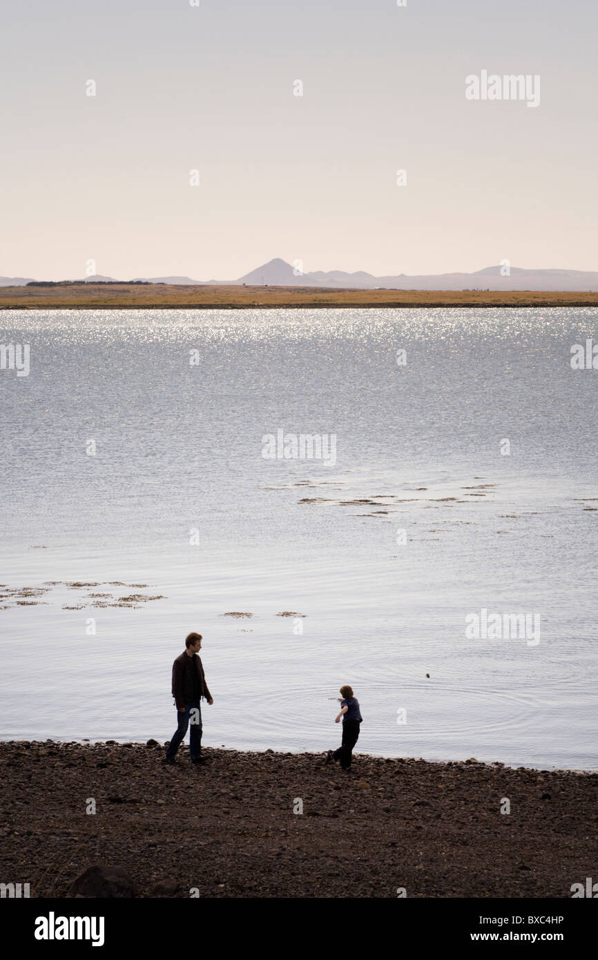 Garçon en train de lancer des pierres dans l'océan, son père est paré. Reykjavik Islande Banque D'Images