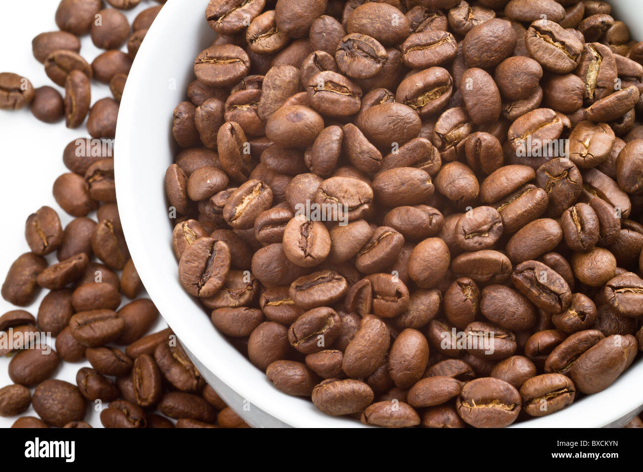 Close up de grains de café dans et autour d'un bol blanc et sur fond blanc Banque D'Images