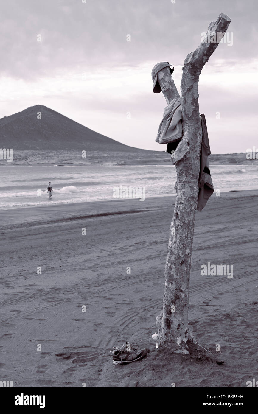 Dans les tons noir et blanc photographie d'un arbre élagué utilisé pour accrocher ses vêtements tandis que le propriétaire nage à El Medano Tenerife Banque D'Images