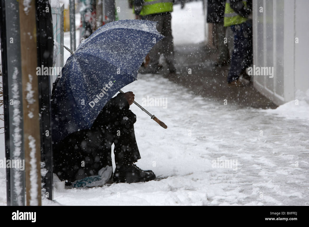 Street mendiant assis sous parapluie deloitte dans la neige sur un jour froid des hivers enneigés de l'Irlande du Nord Belfast Banque D'Images