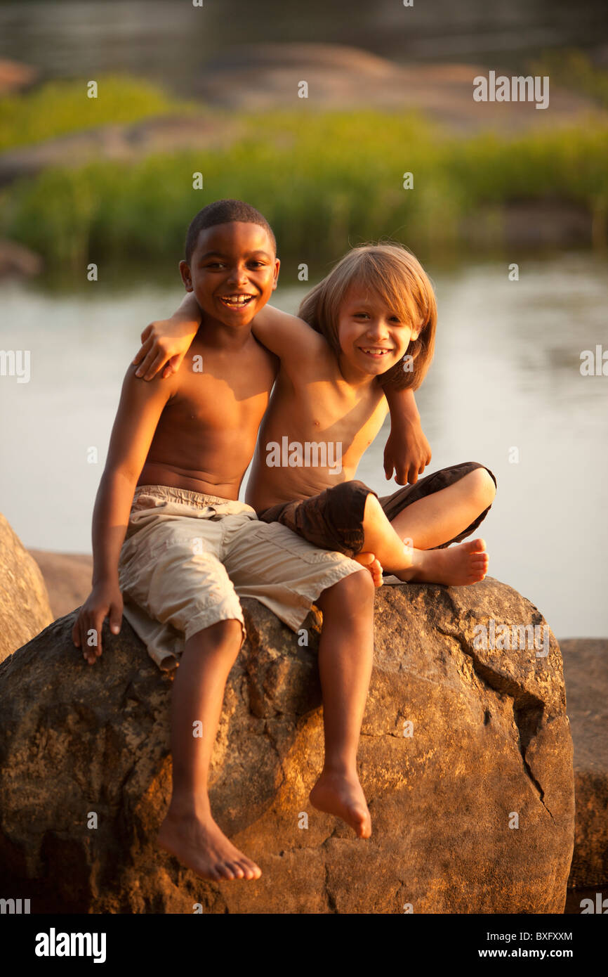Smiling boys hugging on rock près du lac Banque D'Images
