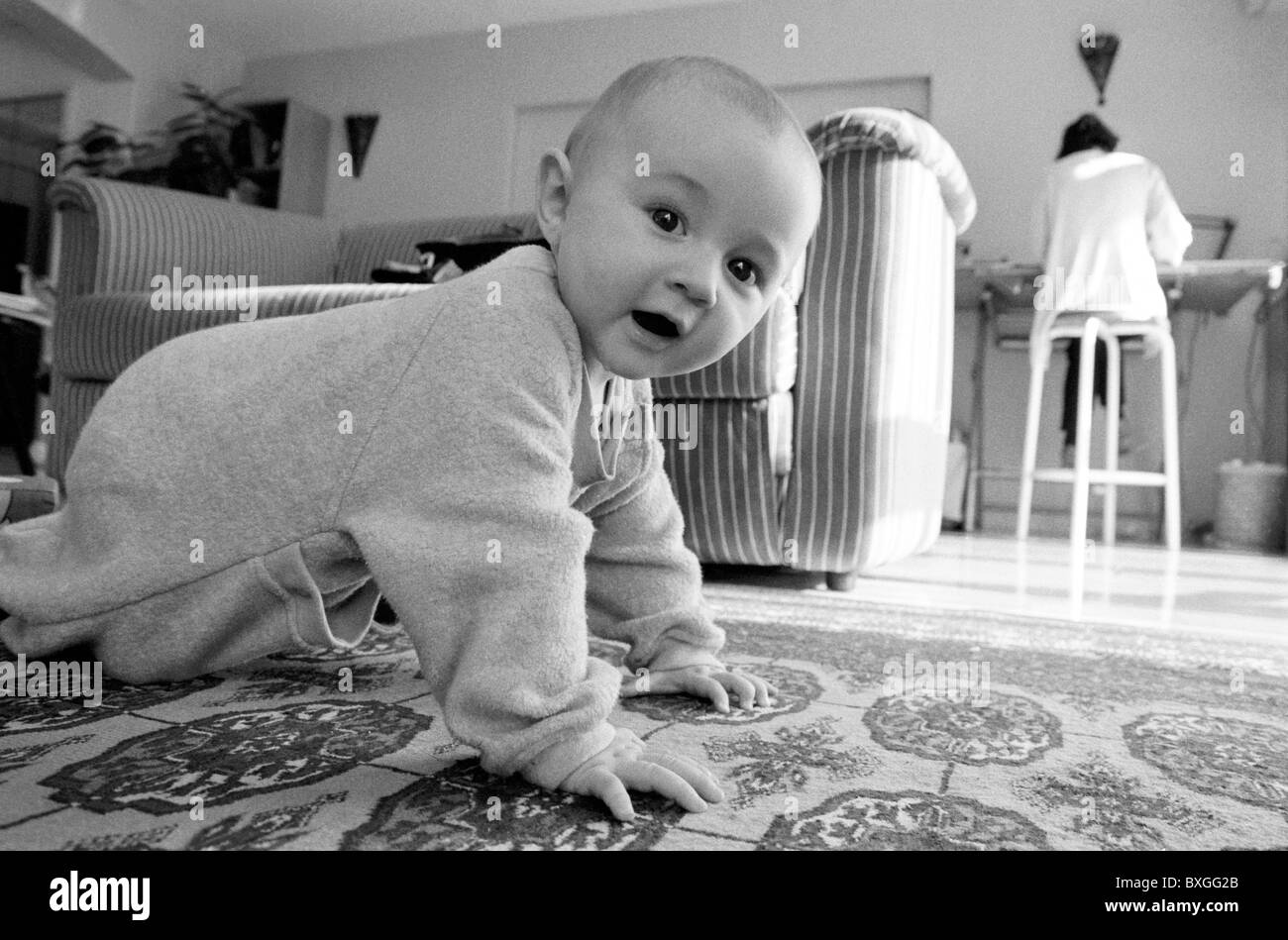 Un an baby girl de ramper sur le tapis de salon pendant que sa mère travaille. Banque D'Images