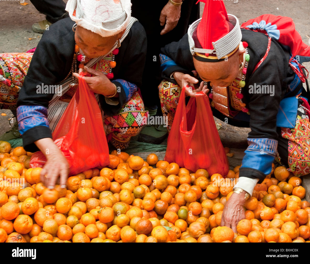L'Asie, Chine, Yunnan, Honghe Préfecture, Jinping. Les femmes Yao tête rouge sélectionner des oranges au marché. Banque D'Images