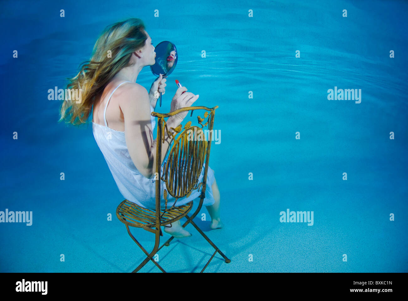 Femme assise sur une chaise et à la recherche dans le miroir sous l'eau Banque D'Images