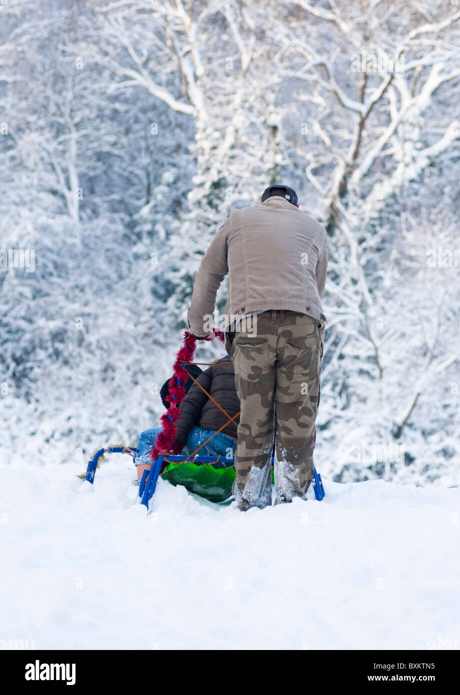 Papa pousse son traîneau d'enfant en bas de la colline dans le Worcestershire, en Angleterre, au cours de l'hiver de 2010. Banque D'Images