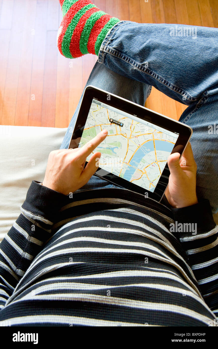 L'homme à la maison à l'aide d'un Apple iPad pour regarder Google maps sur ses genoux. Banque D'Images