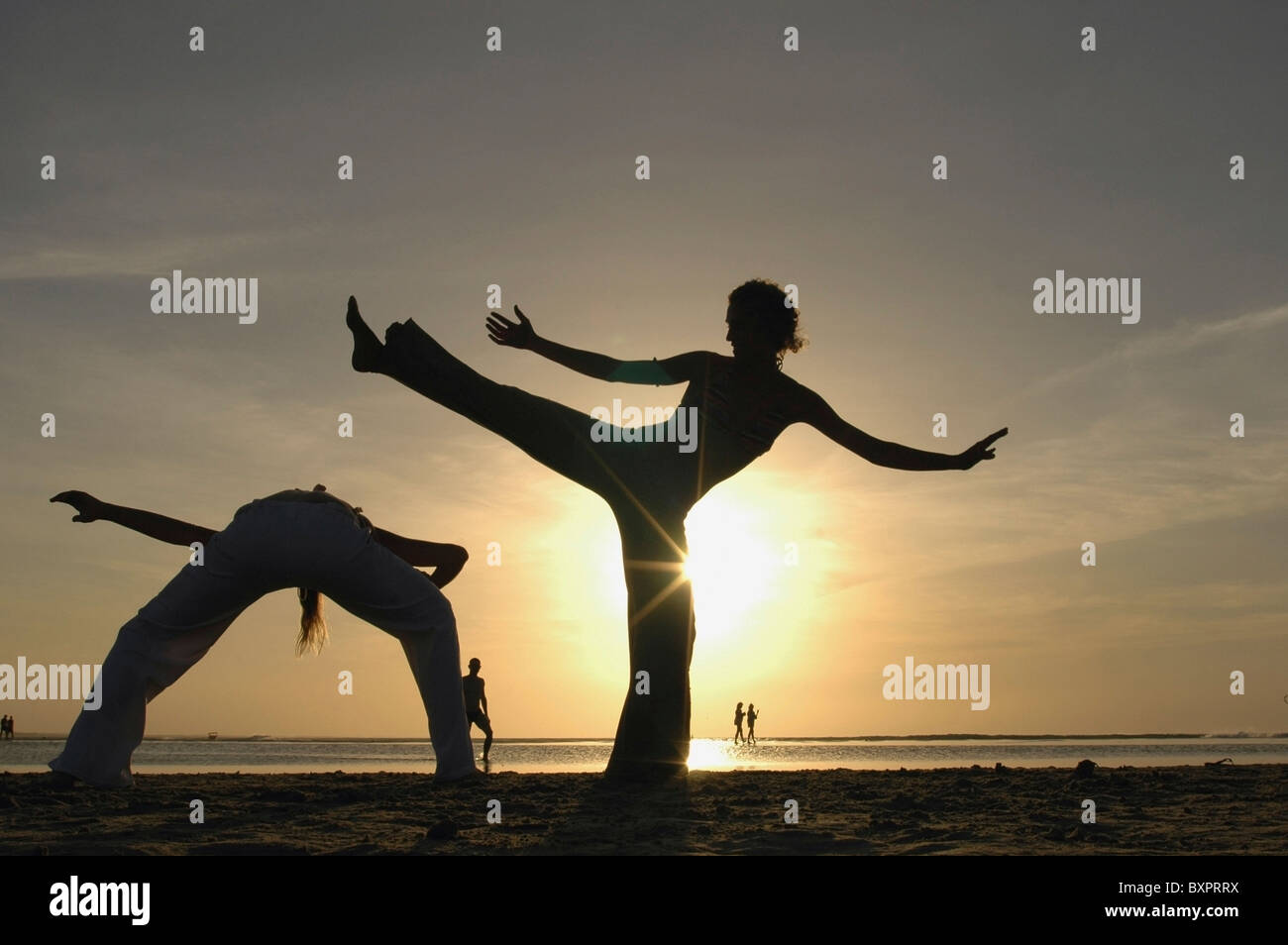 Deux femmes se profilant faisant la Capoeira sur la plage au coucher du soleil Banque D'Images