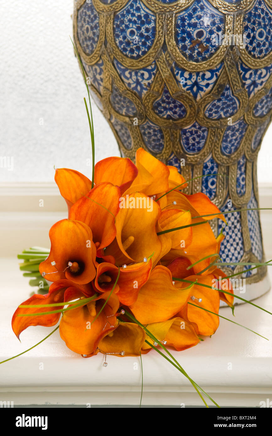 Un bouquet de mariage Calla orange à côté d'un vase de style oriental bleu Banque D'Images